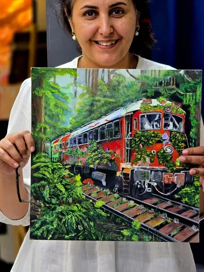 A proud student displays her imaginative gouache painting. We encourage creativity by teaching students to combine technical skill with unique concepts, like this piece where nature reclaims a train.