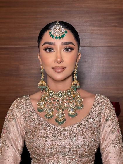 A full view of this gorgeous bride's look, showcasing the flawless base and classic winged liner that perfectly complements her elegant pastel outfit and emerald jewelry.