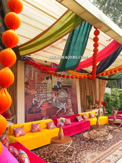 A closer look at the colorful seating arrangement, with patterned cushions and hanging pom-pom garlands adding to the festive 'Banarasia' vibe.