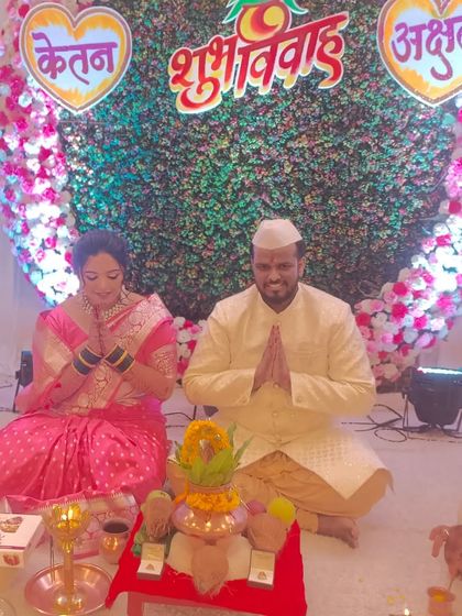 A traditional Maharashtrian 'Shubh Vivah' ceremony. The couple is seated in front of a heart-shaped floral backdrop made of pink and white flowers.