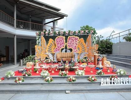 A unique butterfly-themed stage for an outdoor engagement, with large golden butterfly wings filled with flowers.