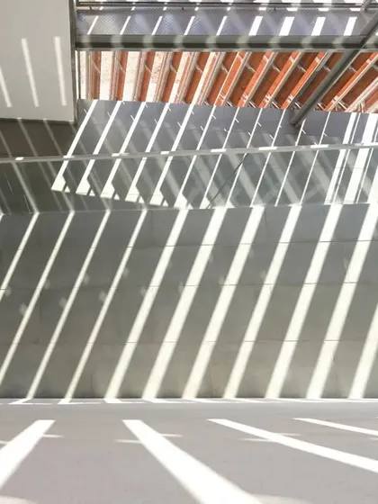 Stripes of sunlight pattern the floor and wall of an interior space at the JSW School of Public Policy. This effect is created by overhead louvers, a key element of our climate-responsive design strategy.