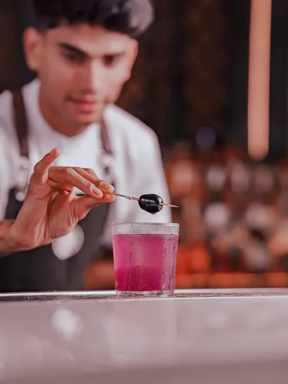 A mixologist carefully garnishes the Jamun Twilight, a work of art that balances the tangy sweetness of the fruit with a zesty lime splash.