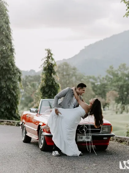 A classic romance scene with a vintage red Mercedes. This shot captures a timeless, movie-like dip against the beautiful hills of Thailand, showing our love for creating iconic, romantic pre-wedding photographs.