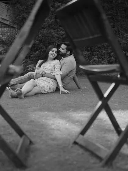 A romantic black and white photo of a couple embracing on the grass, framed creatively to draw the viewer's eye.