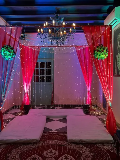A cozy and traditional low-seating arrangement (baithak) with mattresses and bolsters, decorated with a canopy of drapes, fairy lights, and a chandelier.