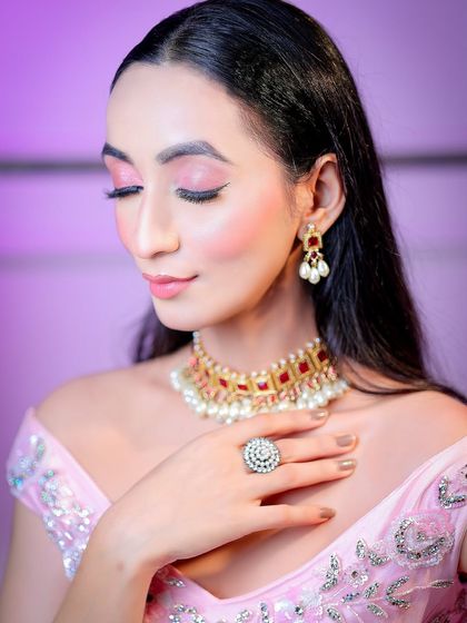 A close-up beauty shot with a purple-lit background, focusing on the makeup and delicate jewelry.
