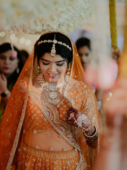 Reeya walked down the aisle for her beautiful sunset Varmala in this gorgeous orange lehenga. We paired it with a fresh matte face, copper-hued eyes, and blooms in her bun that matched her outfit, creating a stunning Marwadi bridal look.
