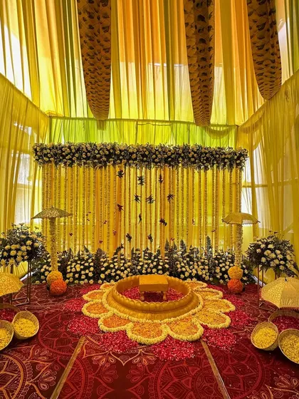 An intimate and traditional Haldi seating area. We created a flower-shaped arrangement on the floor with marigold petals and a backdrop of hanging floral strings and decorative umbrellas.