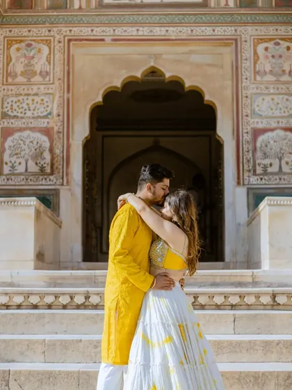 A romantic embrace in front of the detailed facade of a Jaipur palace. The groom's bright yellow kurta and the bride's coordinated lehenga bring a joyful energy to this royal pre-wedding photo.