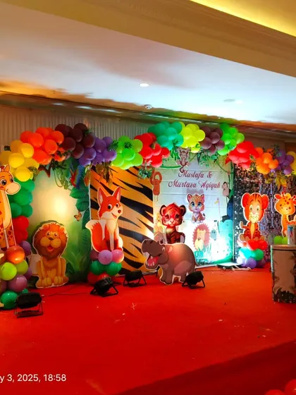 The full stage setup for a jungle-themed celebration, with a red carpet, marquee letter 'M', and a variety of animal props.