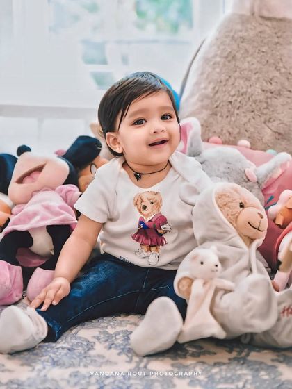 A happy toddler sits in a sea of stuffed animals. This playful setup at home results in adorable and fun portraits that capture the joy of childhood.