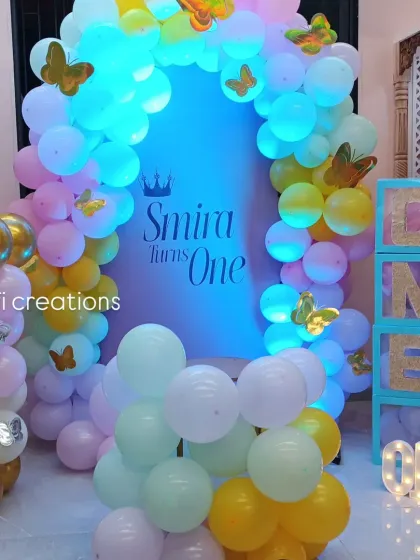 A beautiful butterfly-themed first birthday party. This home setup features a pastel balloon arch adorned with golden butterflies, "ONE" display boxes, and a light-up number.