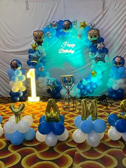 A Boss Baby themed first birthday decoration, featuring a blue and white ring backdrop, marquee number '1', and the name spelled out with balloon letters.
