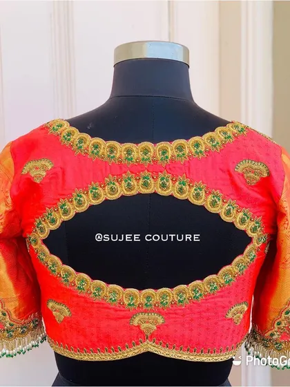The back of a vibrant coral pink blouse with an oval keyhole cutout. The design features green and gold embroidered motifs and contrasting gold brocade sleeves.