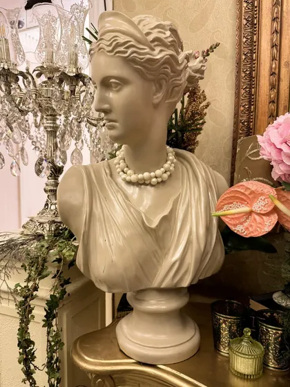 A classical Grecian bust adorned with a string of pearls, set beside a crystal chandelier, blending classical art with opulent wedding decor.