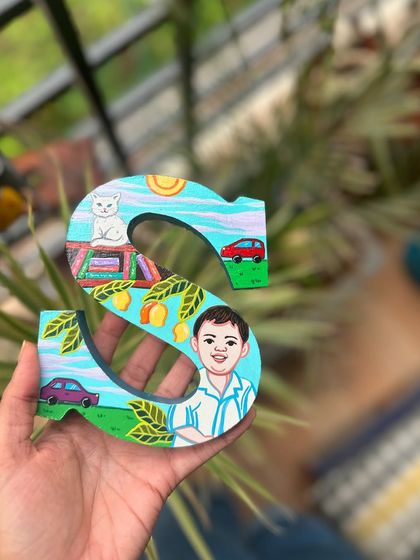 A custom wooden letter 'S' painted for a child, featuring his portrait, his cat, and his favorite toys.