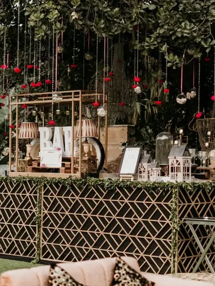 An elegant outdoor bar setup perfect for a sophisticated evening reception. The geometric bar front, combined with hanging floral decor and warm lighting, creates a chic and inviting space for guests.