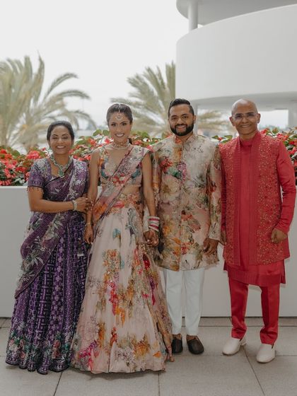 A closer look at the groom's family. The groom's floral sherwani is beautifully framed by his mother's purple bandhani lehenga and his father's vibrant red kurta set. This demonstrates our approach to individual styling within a group, ensuring each person feels confident and celebrated.