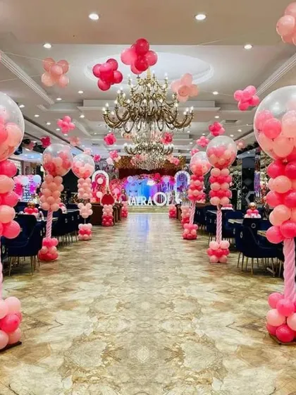 A grand walkway decoration for a large event. The hall is lined with elaborate pink balloon pillars, creating a stunning entrance for guests.