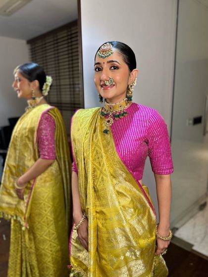 A full-length view showing Archi's complete look. The sleek bun adorned with flowers and the elegantly draped saree create a look of classic, traditional beauty.