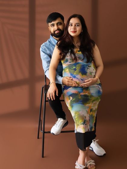 A contemporary couple's portrait with the mom-to-be in a colorful, abstract-print dress, seated on her partner's lap.
