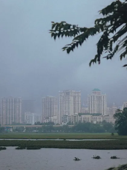 The iconic Hiranandani buildings in Powai seen across the lake on a rainy day. The scene is soft and serene, a perfect example of urban nature.