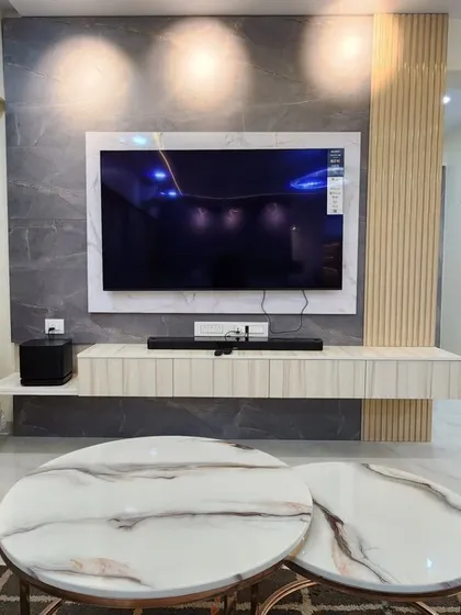 A close-up of a floating TV unit against a grey marble-finish wall panel. The nested marble-top coffee tables add a touch of modern luxury.