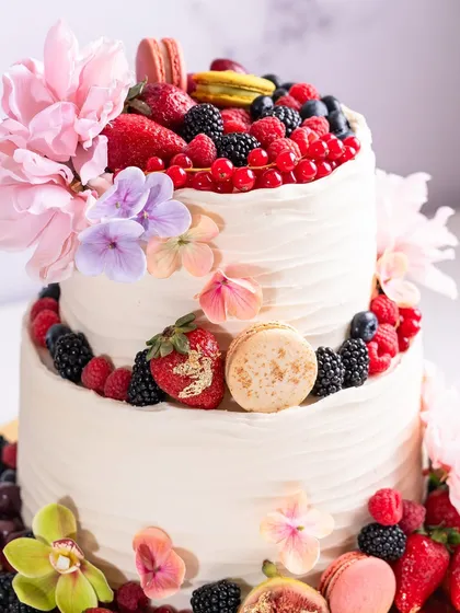 A full view of the stunning two-tiered cake, adorned with a cascade of fresh berries, macarons, and delicate flowers.