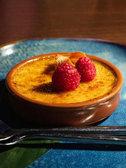 A beautiful crème brûlée garnished with fresh raspberries. The vibrant fruit adds a pop of color and a sense of freshness to the classic dessert.