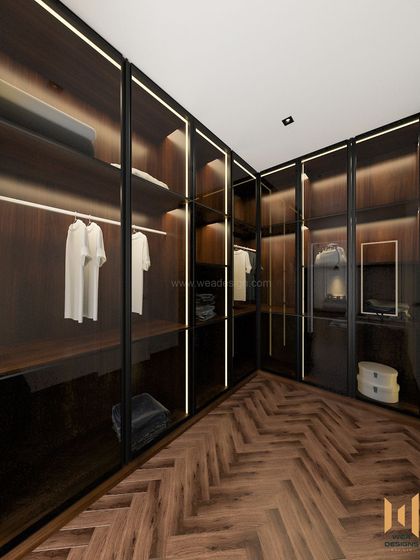 A luxurious walk-in closet with dark wood, glass doors, and integrated profile lighting, creating a high-end boutique feel.
