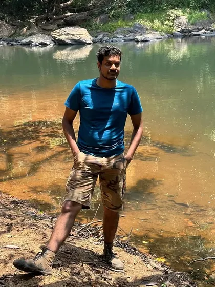 The trek leader posing by the calm river, enjoying a moment of peace during a summer trek.