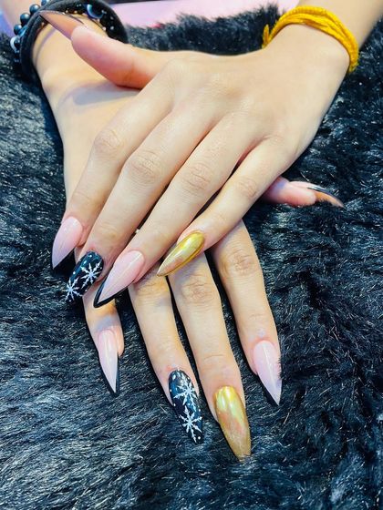 A wintery mix of textures and art. This set combines a stunning gold chrome nail with black nails featuring hand-painted white snowflakes, all on sharp, long stiletto nails.