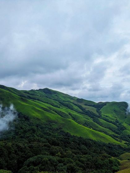 The rolling green hills of the Netravathi range under a cloudy sky.