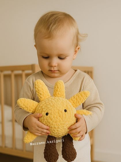 A child holding our cheerful sun-shaped plush toy. Made with baby-safe chunky yarn, it's designed to bring a little sunshine and happiness.