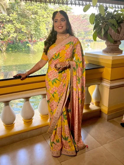 A full-length shot of the bride at her Haldi, looking beautiful in a floral saree and fresh makeup.