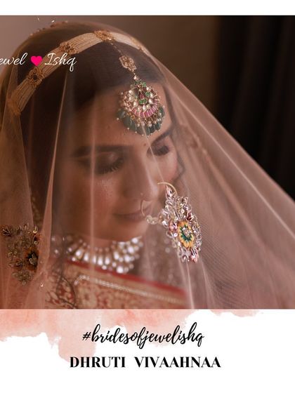 A beautiful shot of the bride through her veil, focusing on the intricate nath and maang tikka.