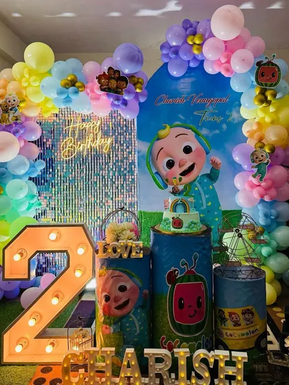 A vibrant Cocomelon themed party for Charish's second birthday, featuring a colorful balloon arch, a shimmery backdrop, and large character cutouts.