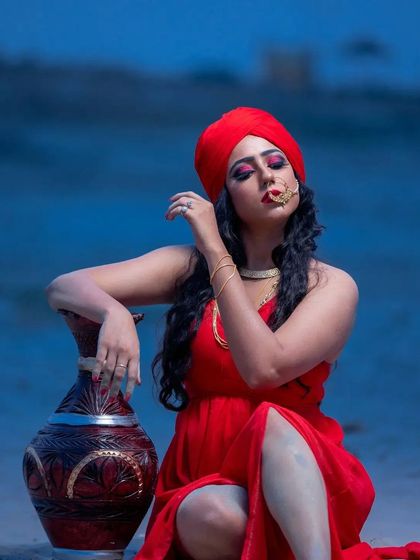 A powerful pose from the desert shoot. The makeup features intense, dark pink eyeshadow and a bold nath, which stands out against the vibrant red of the turban and dress.