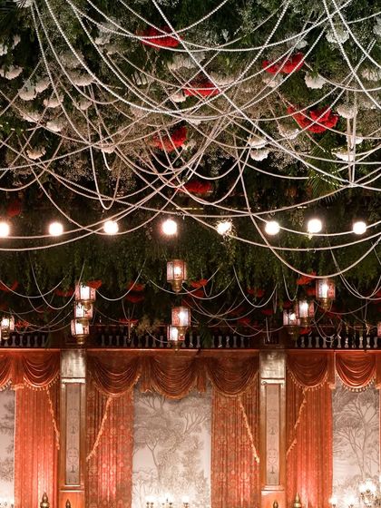 The ceiling treatment for this grand reception featured a dense canopy of greenery, red roses, and hanging lanterns, creating a dramatic and opulent effect.