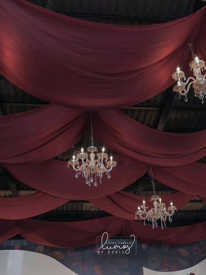 A stunning wedding stage with a ceiling of rich burgundy draping and multiple crystal chandeliers. The design exudes luxury, romance, and timeless elegance.