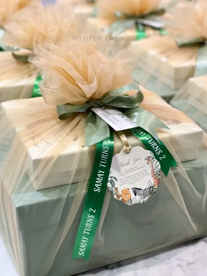 A close-up of the safari return gift packaging. The custom ribbon reads 'Samay Turns 2' and the tag features a thank you message with matching jungle animal artwork, ensuring every detail is on-theme.
