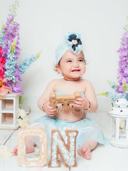 A first birthday portrait with a floral theme. The colorful flowers and 'ONE' sign create a beautiful and celebratory setting.