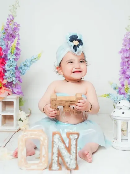 A first birthday portrait with a floral theme. The colorful flowers and 'ONE' sign create a beautiful and celebratory setting.
