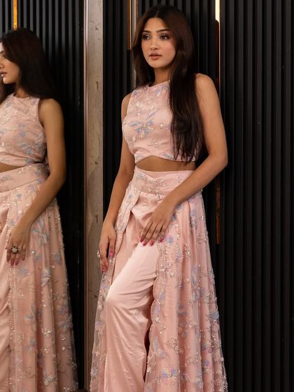 This soft pink Indo-Western outfit features pants under a sheer, embroidered skirt. It's a unique and trendy choice for a fashion-forward guest at a sangeet or reception.