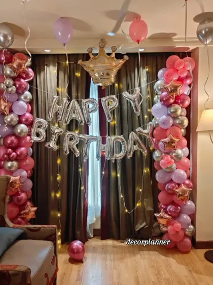 A close-up of the main decoration area for the Pinterest-inspired birthday. The two balloon pillars in shades of pink, purple, and silver frame the 'Happy Birthday' foil balloons and a cute crown, fit for a queen.