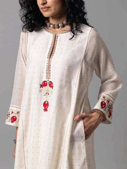 A close-up of an off-white kurta with delicate red and green pomegranate embroidery on the cuffs and placket, a subtle nod to traditional motifs.