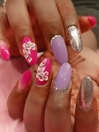 A playful and colorful set combining pink ombré with 3D flowers, solid lavender nails with rhinestone cuticles, and full-coverage gold glitter nails.