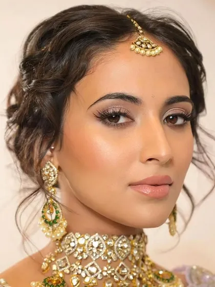 A close-up on a trendy tousled updo. This style has soft, face-framing tendrils and a textured finish, making it a perfect choice for a modern bride wearing a pastel lehenga.
