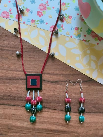 This necklace set features a fabric pendant with colorful thread-wrapped beads. The matching long earrings complete the look, making it an easy choice for Durga Puja or Navratri celebrations.